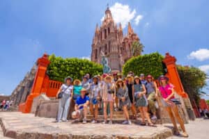 Un grupo de personas posan juntas frente a la iglesia Parroquia de San Miguel Arcángel, de estilo gótico rosa, en San Miguel de Allende, México, después de asistir a eventos de conferencias en hoteles y complejos turísticos cercanos en un día soleado.
