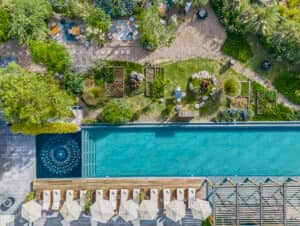 Vista aérea de una piscina rectangular en uno de los mejores complejos turísticos de México, con sombrillas blancas y tumbonas a lo largo de un lado, bordeada de exuberantes jardines verdes; perfecta para relajarse después de eventos de conferencias o reuniones de hotel.