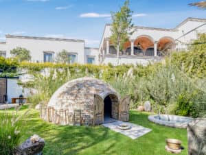 Una cúpula redonda de ladrillo con puertas dobles de madera se alza en un exuberante jardín de uno de los resorts más exclusivos de México, rodeada de vegetación y tumbonas. Cerca de allí, una piscina circular complementa el entorno perfecto para reuniones o conferencias.