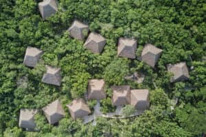Vista aérea de varias cabañas con techo de paja dispuestas entre densos árboles verdes, conectadas por senderos serpenteantes a través del frondoso bosque: un entorno idílico para reuniones o eventos de conferencias en complejos turísticos de México.