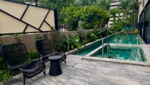 Moderna zona de piscina al aire libre en uno de los mejores resorts de México, que cuenta con un pequeño jacuzzi, una piscina larga, tumbonas de mimbre y exuberante vegetación, perfecta para relajarse después de eventos o reuniones de negocios.
