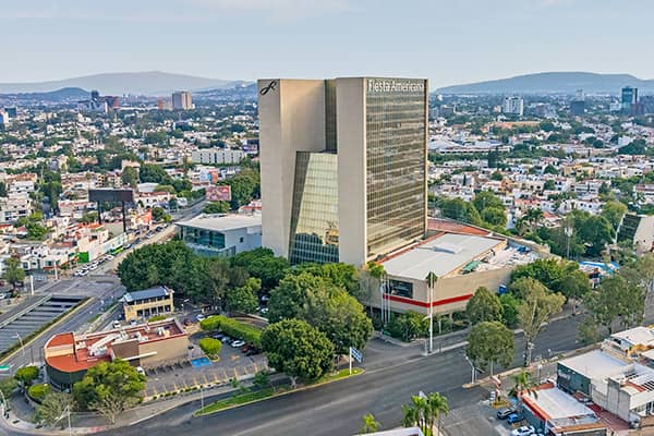 Aerial view of the Fiesta Americana hotel, a tall modern building surrounded by trees and city streets, ideal for meetings and conference events, with Mexico’s vibrant urban landscape and hills in the background.