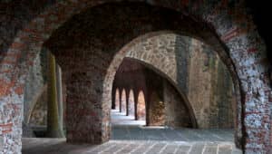 Arcos y columnas de piedra en un edificio antiguo con texturas de ladrillo y piedra, que crean una serie de arcos y sombras que se repiten a lo largo de un suelo de baldosas, perfecto para eventos de conferencias o reuniones memorables en hoteles históricos de México.