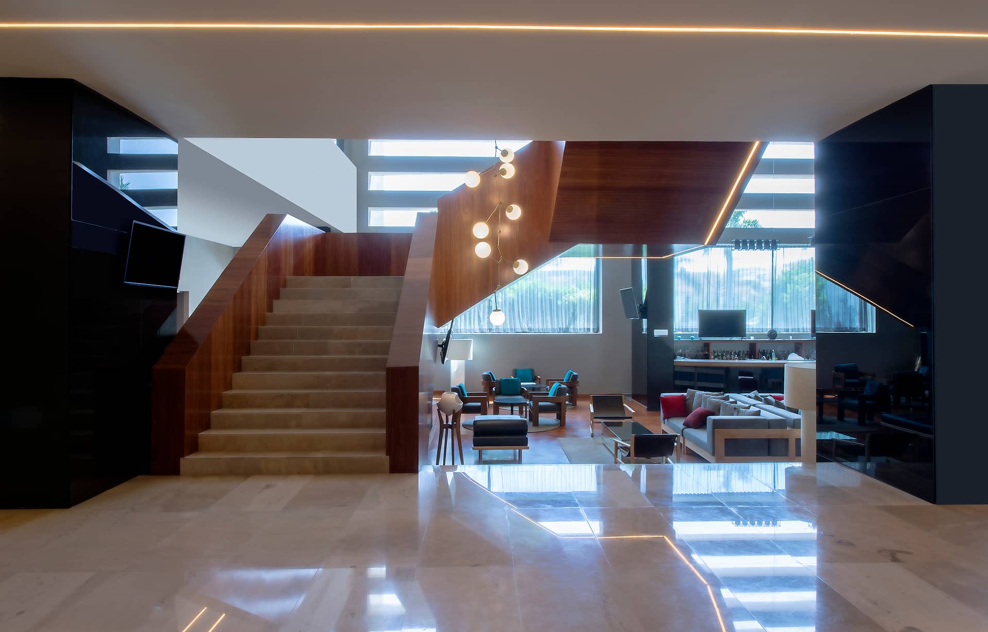 Modern hotel lobby with polished marble floors, a wide staircase with wooden paneling, contemporary seating areas, and large windows—ideal for Mexico hotels hosting meetings or conference events in stylish comfort.