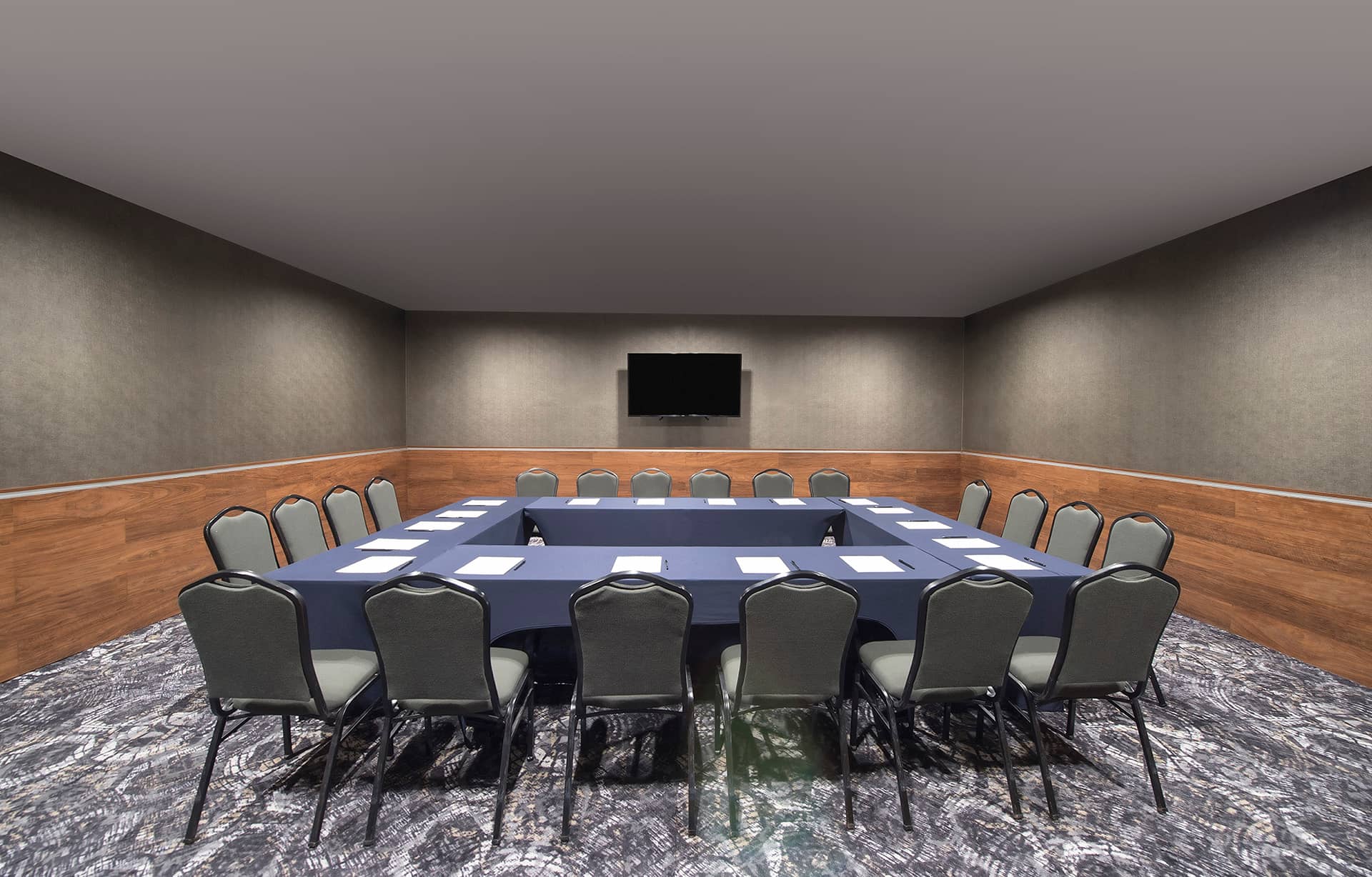 Ideal for meetings and conference events, this resort's Mexico hotel features a U-shaped conference room with blue tablecloths, notepads, and pens at each seat. A flat-screen TV sits up front, complemented by patterned carpet and neutral walls.
