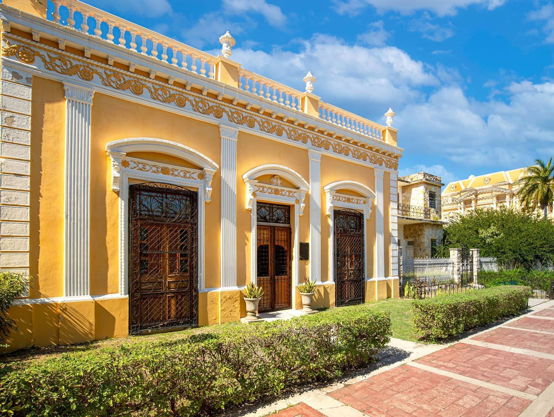 A historic yellow and white colonial-style building with ornate details, large arched windows with wrought iron grilles, and potted plants at the entrance—an ideal setting for memorable conference events or meetings in Mexico.
