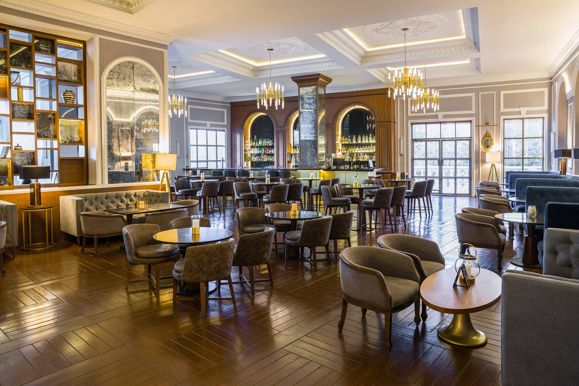 Elegant hotel lounge with polished wooden floors, round tables, and cushioned chairs—ideal for meetings or conference events. Chandeliers and a stylish bar add charm, while large windows fill Mexico resorts’ hotels with warm natural light.