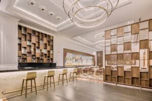 Interior de restaurante moderno y elegante con techo alto, lámparas colgantes circulares y una barra con cuatro taburetes: ideal para reuniones o eventos en resorts de lujo en México. La iluminación cálida y tenue, junto con obras de arte llamativas, crean un ambiente acogedor propio de un hotel.