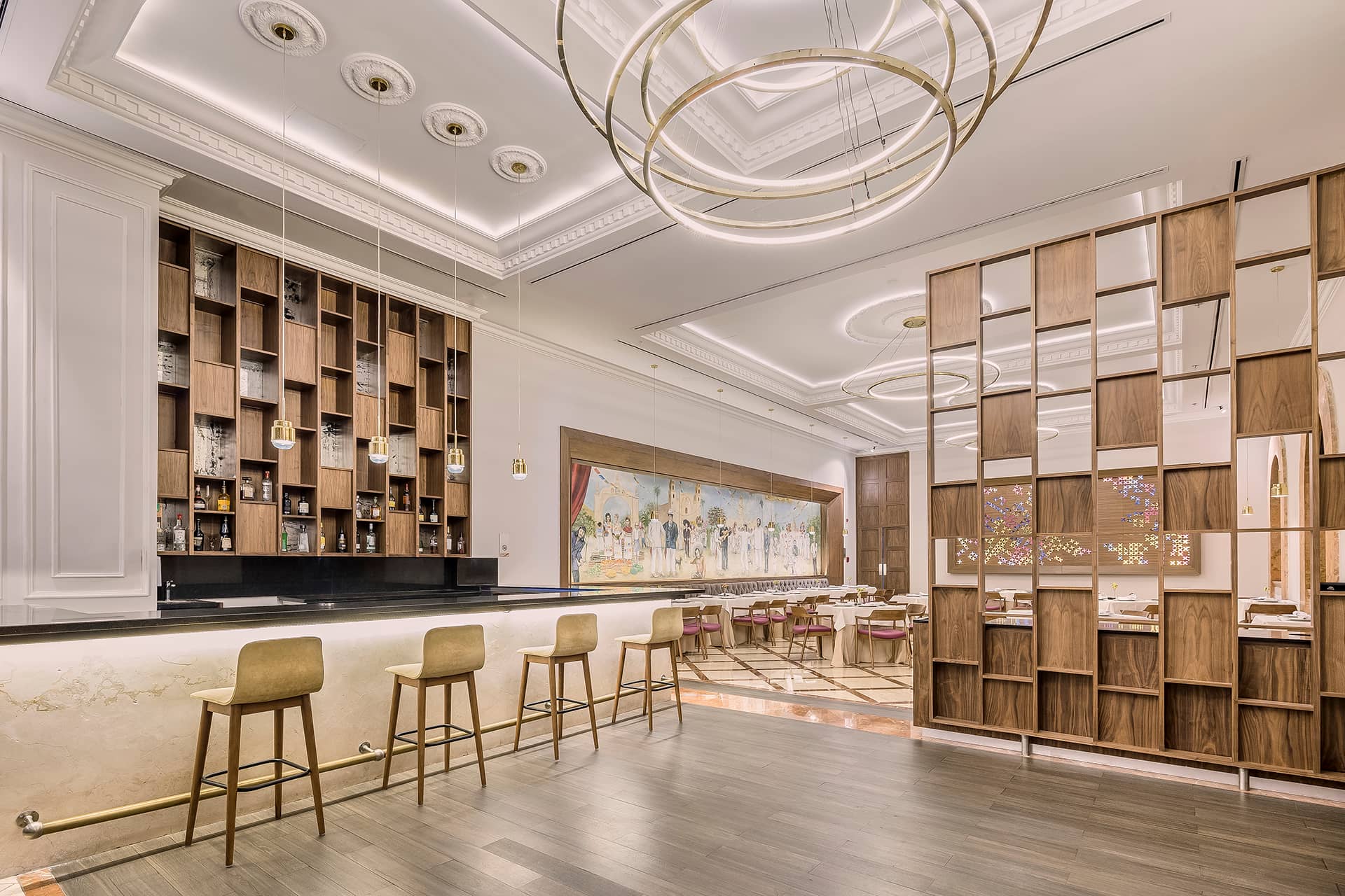 Modern, elegant restaurant interior with a high ceiling, circular pendant lights, and a bar with four stools—perfect for meetings or conference events at upscale Mexico resorts. Soft, warm lighting and striking artwork create an inviting hotel atmosphere.