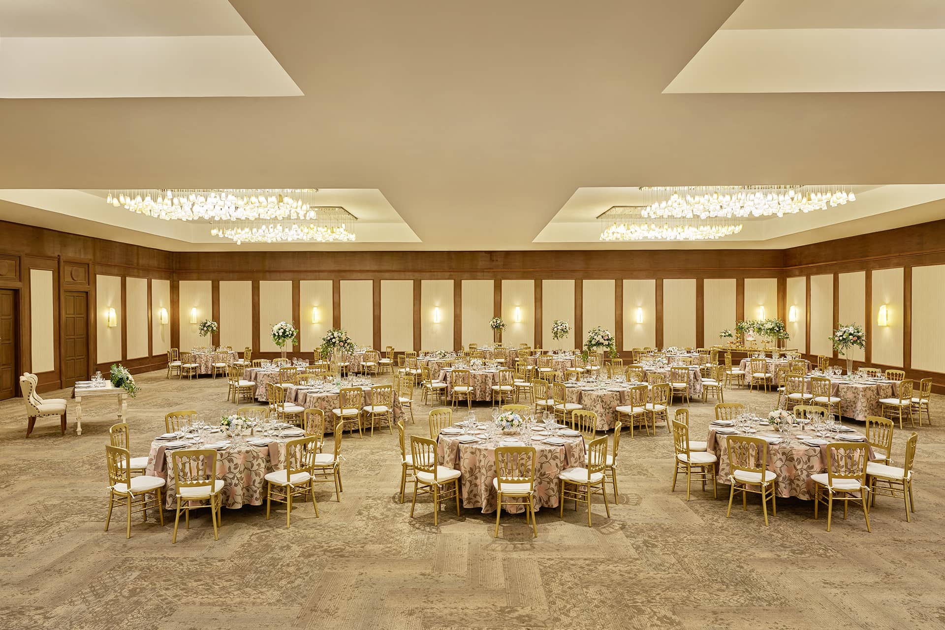 Large, elegant banquet hall with round tables covered in patterned cloths, gold chairs, floral centerpieces, and soft lighting from modern chandeliers—perfect for meetings or conference events at top resorts and hotels in Mexico.