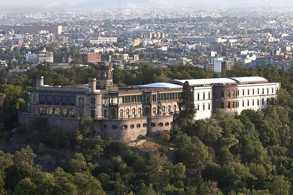 Aerial view of Chapultepec Castle surrounded by trees, with the cityscape of Mexico City in the background—an iconic location near top Mexico hotels and resorts, ideal for conference events and meetings under a clear sky.