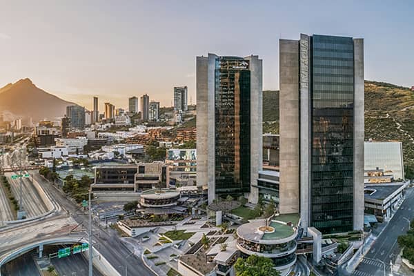 Aerial view of a modern cityscape with tall glass skyscrapers, luxury hotels, a highway, and mountains in the background at sunset—an ideal destination for conference events or meetings in Mexico.