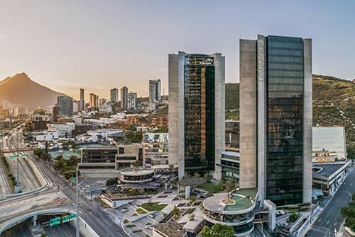 A modern cityscape at sunset with tall glass skyscrapers, smaller buildings, highways, and a mountain in the background under a clear sky—perfect for conference events or business meetings at top Mexico hotels and resorts.