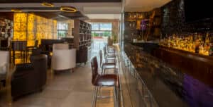Moderno bar y salón en uno de los resorts más exclusivos de México, con barra de mármol, taburetes de madera, iluminación ambiental y asientos elegantes: ideal para reuniones o eventos. Grandes ventanales inundan el espacio de luz natural para los huéspedes del hotel.