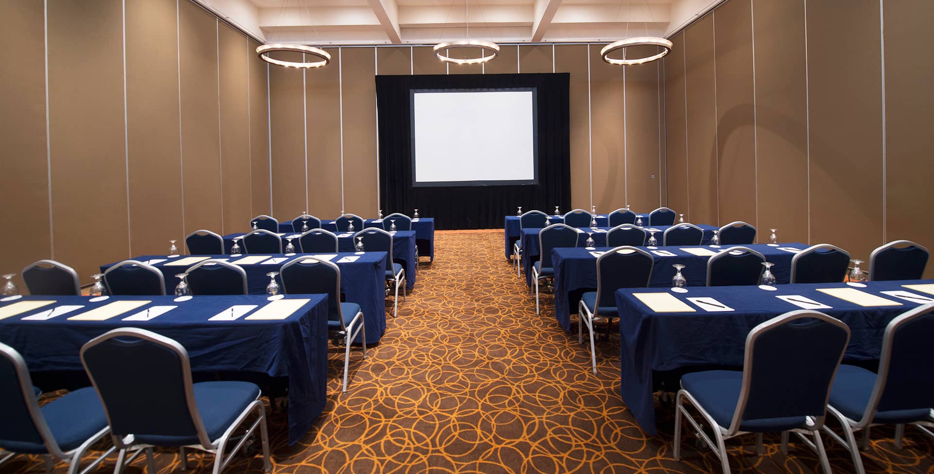 Rows of tables and chairs with navy blue covers are arranged classroom-style in a conference room at one of Mexico’s top resorts, perfect for meetings and conference events, with notepads, pens, and water glasses on each table.