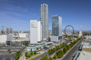 Un paisaje urbano moderno con altos rascacielos, incluido el hotel Grand Fiesta Americana, uno de los principales complejos turísticos de México para reuniones y eventos de conferencias, una gran noria, estacionamientos y amplias avenidas bajo un cielo azul despejado.