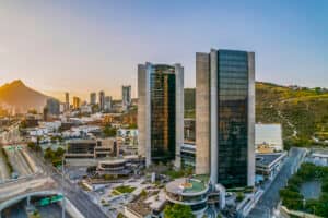 Vista aérea de modernos rascacielos y hoteles cercanos al amanecer en una ciudad con montañas al fondo, amplias avenidas y espacios verdes, ideal para eventos o reuniones en los vibrantes centros turísticos de México.