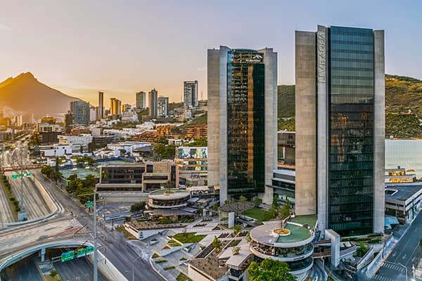 Aerial view of a modern cityscape at sunset, featuring tall glass skyscrapers, busy roads, smaller buildings, and a mountain in the background—an ideal spot for vibrant conference events or meetings at top Mexico hotels and resorts.