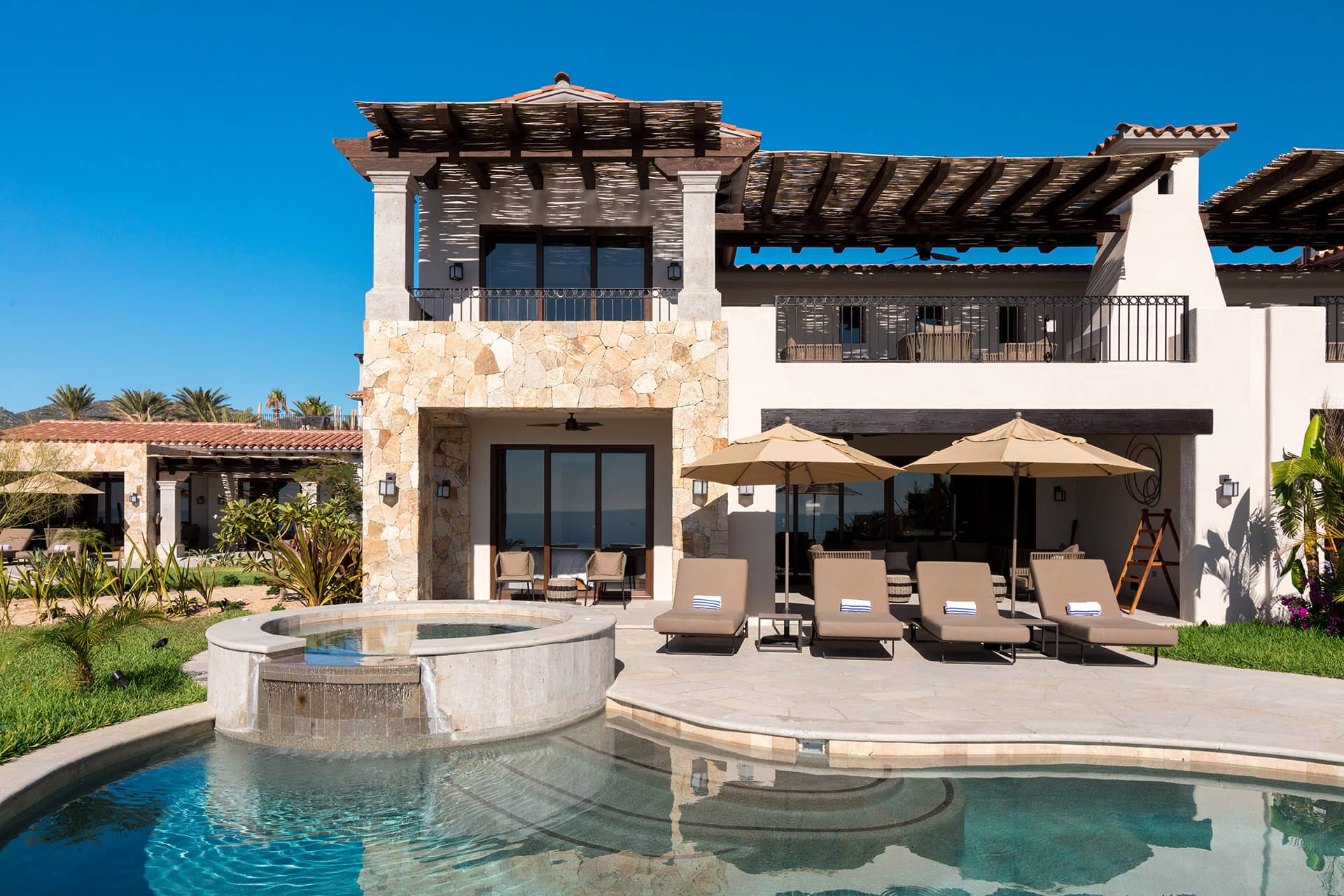 A luxurious villa with stone and stucco exterior, shaded balconies, poolside lounge chairs, and a circular hot tub beside a swimming pool—perfect for relaxing after conference events at one of Mexico’s premier resorts.