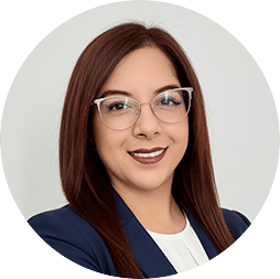 Mujer profesional de cabello castaño liso, con gafas transparentes, chaqueta azul marino y blusa blanca, sonriendo con confianza sobre un fondo gris claro; ideal para promocionar eventos o reuniones en hoteles y complejos turísticos de México.