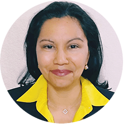Una mujer de cabello oscuro de longitud media, vestida con un blazer negro con cuello amarillo brillante y un collar de color claro, sonríe a la cámara sobre un fondo claro; un atuendo perfecto para los eventos de conferencias en hoteles de México.