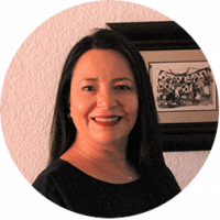 A woman with long dark hair and a black top smiles at the camera. She stands indoors at a Mexico hotel, in front of a textured white wall and framed black-and-white artwork—an inviting scene for conference events or meetings.