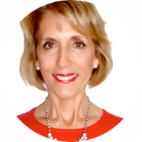 Smiling woman with short blonde hair wearing a bright red top, a pearl necklace, and pearl earrings, pictured against a plain white background—perfect for promoting meetings or conference events at Mexico hotels and resorts.