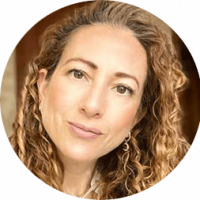 A woman with long, curly light brown hair and light skin looks into the camera with a neutral expression. She is wearing earrings and a light top, set against a softly blurred background at one of Mexico’s premier conference resorts.