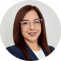 Professional woman with straight brown hair, wearing clear eyeglasses, a navy blazer, and a white top, smiling confidently against a light gray background—ideal for promoting conference events or meetings at Mexico hotels and resorts.