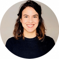 A woman with shoulder-length brown hair, wearing a dark textured sweater, smiles at the camera against a plain light background—perfect for professional profiles or conference events promotions.